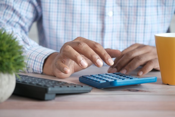 Mãos digitando em uma calculadora sobre a mesa